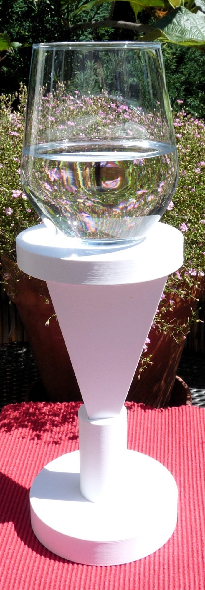 Die Podestpyramide steht umgedreht in einem Halter. Au ihrem Podest steht ein Glas mit Wasser das kraftvoll energetisiert wird.