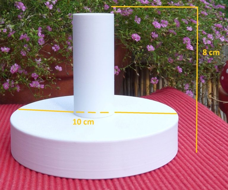 Ein Halter für eine Podestpyramide mit eingezeichneten Maßen auf einem Gartentisch mit blühenden Blumen.