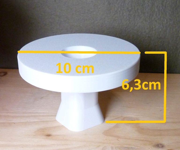 Ein Halter für eine Podestpyramide mit eingezeichneten Maßen auf einem Gartentisch mit blühenden Blumen.